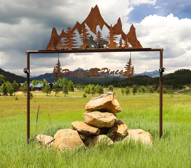 Rusted metal Piedra Pines entry sign with a bear, pines and mountains, San Juan peaks behind