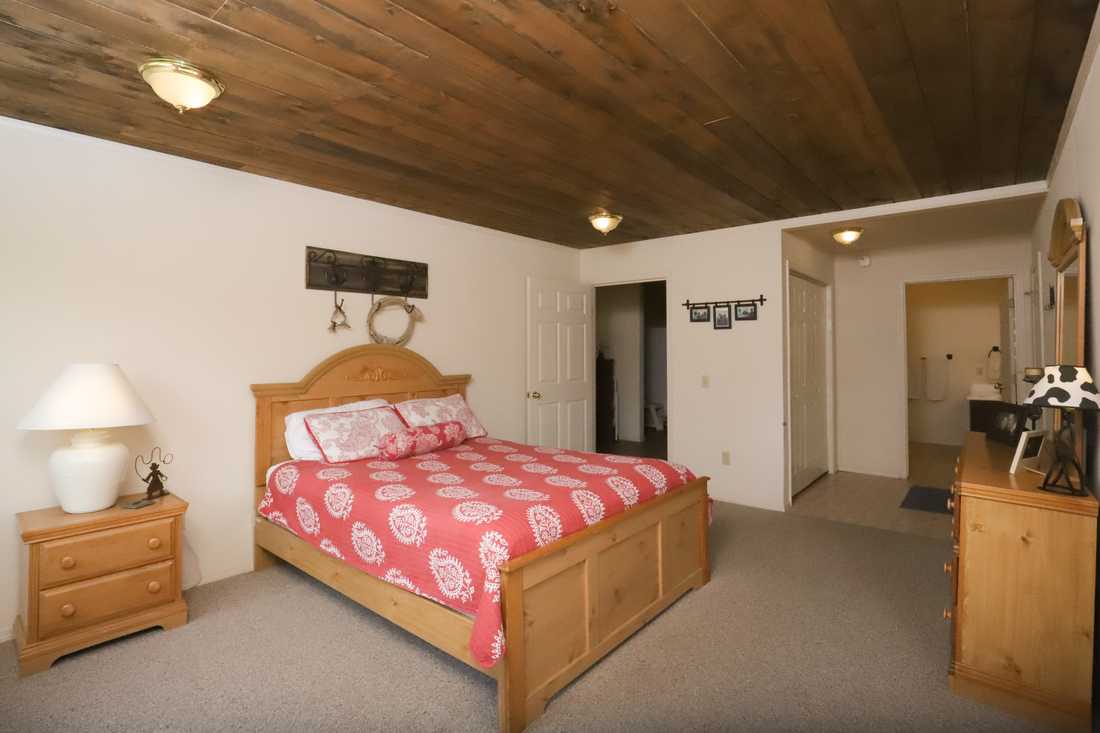 Main-floor queen bedroom with a wood-plank ceiling and pine furniture